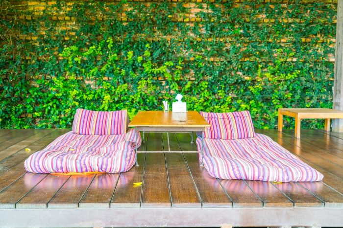 What Happens If You Don’t Clean Your Outdoor Patio and Deck? | What If Series 4 Vibrant outdoor patio setup with striped cushions, a wooden table, and lush green ivy-covered wall, emphasizing the importance of regular patio and deck cleaning for maintaining appearance and safety.
