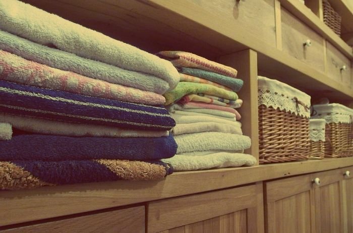 Neatly folded towels and organized storage baskets on wooden shelves, illustrating the misconception that fortnightly or monthly cleaning saves money, despite the increased cost of removing built-up dirt over time.