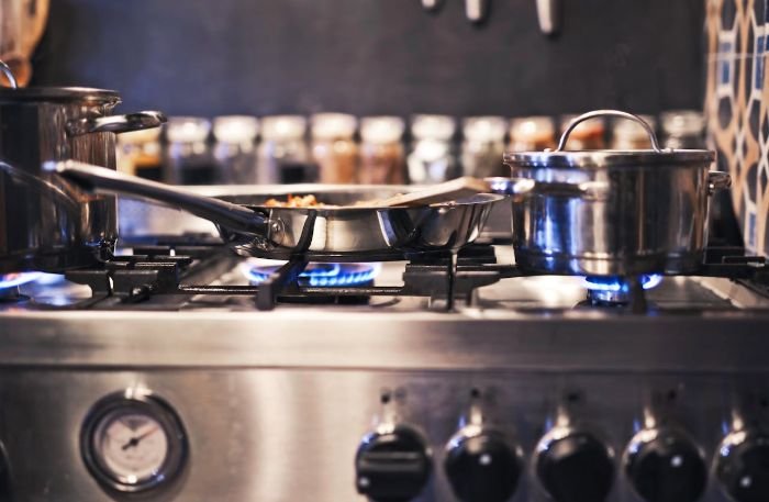 Stainless steel gas stove with pots and pans, illustrating the health risks of neglected kitchen appliances, including bacteria, mold, and cross-contamination.