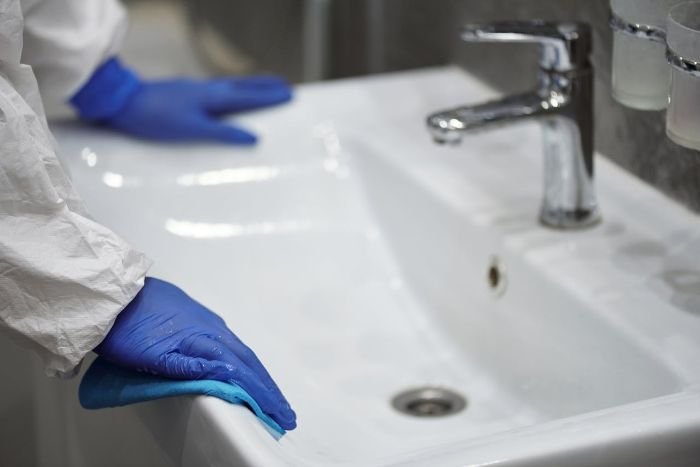 Person in protective gear cleaning a sink, representing professional move-out cleaning services