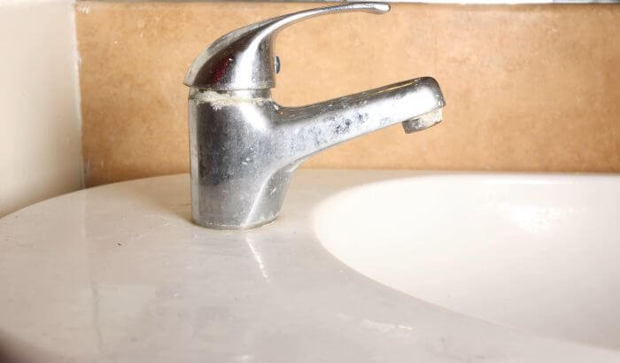 Close-up of a bathroom faucet with visible limescale buildup, illustrating how to remove limescale from your home