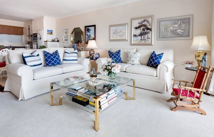 Bright, well-kept living room with white sofas and glass coffee table, illustrating how fortnightly cleaning can lead to deep-set stains and dust build-up if not addressed with regular weekly cleanings.