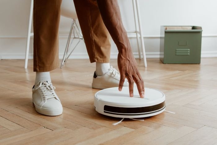 Person adjusting a smart robotic vacuum on a hardwood floor for optimal setup and performance.