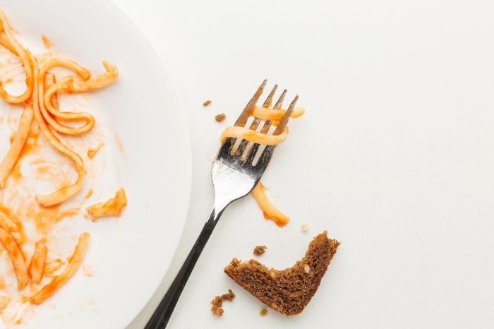 Fork with pasta sauce and bread crumbs on a plate, symbolizing sticky residue and visible stains that can accumulate in a refrigerator without regular cleaning.