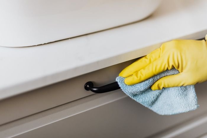 Hand in a yellow glove wiping a cabinet handle with a microfiber cloth, illustrating time-saving cleaning techniques