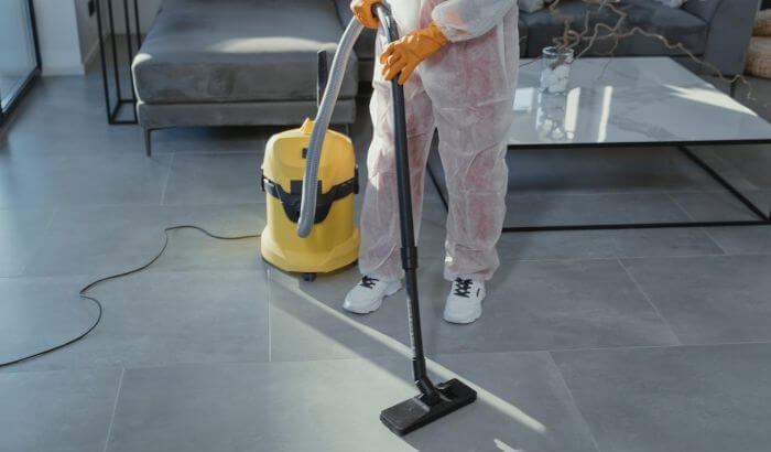 Professional cleaner using a vacuum on tiled floor, emphasizing the advantages of weekly cleaning for a consistently spotless home.