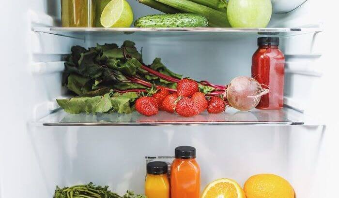 Open refrigerator filled with fresh fruits, vegetables, and juices, emphasizing the importance of regular cleaning for food safety and hygiene.