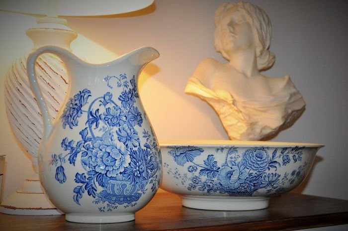 Antique porcelain pitcher and bowl with floral designs on a wooden surface, symbolizing the need for careful handling of fragile and valuable items during cleaning.