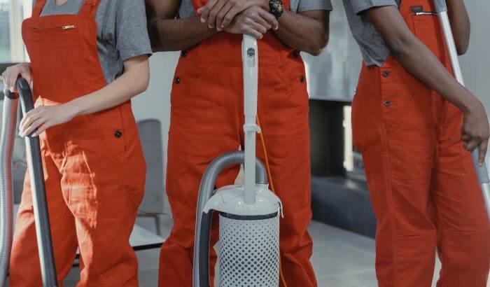 Professional cleaning team in orange uniforms holding modern cleaning tools, including a vacuum cleaner, showcasing the best cleaning tools for busy professionals.