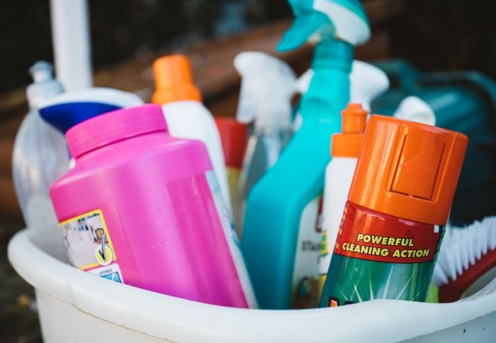 Various cleaning products in a white bucket, illustrating the importance of using the correct amount and type for effective cleaning.