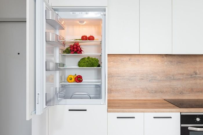 An open refrigerator with fresh vegetables inside, highlighting the importance of cleaning fridge seals where moisture and food residue can accumulate, creating a breeding ground for bacteria like E. coli and Salmonella.