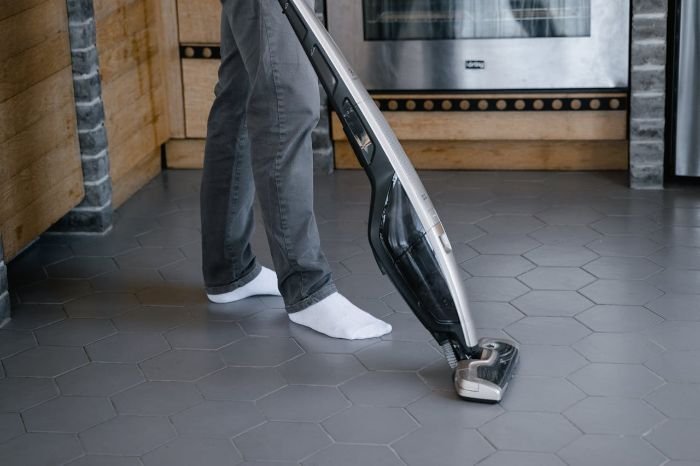 Person using a handheld vacuum cleaner on a tiled kitchen floor to quickly clean up spills and crumbs, ideal for busy spaces.