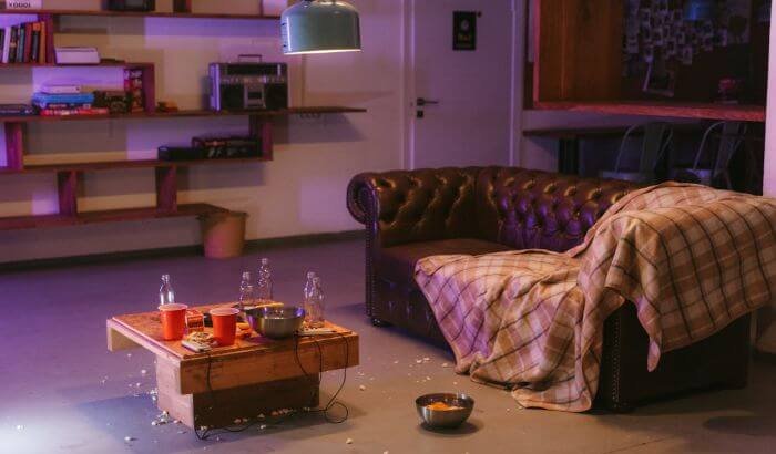 A cluttered and untidy living room with an unclean table, scattered popcorn, and an unkempt couch, highlighting the risks of neglecting regular home cleaning.