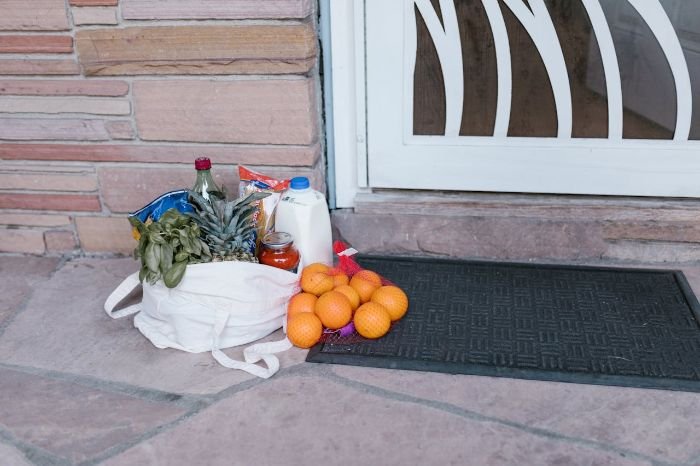 A reusable grocery bag filled with groceries, including fruits, milk, and vegetables, placed on a doorstep. Highlights the potential risk of cross-contamination and the importance of cleaning reusable bags to prevent bacteria from spreading.