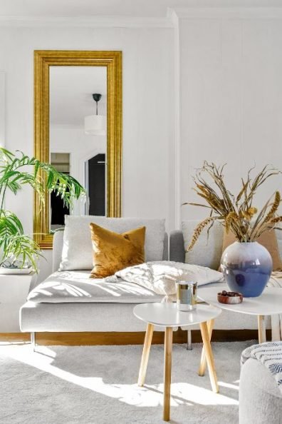 A bright and elegant living room with a stylish sofa, gold-framed mirror, and decorative plants, representing a professionally cleaned home in Mortlake, SW14.