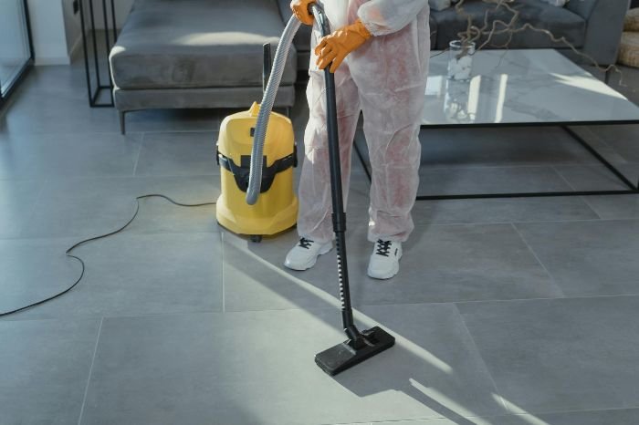 A professional cleaner in protective gear using an industrial vacuum to deep clean a tiled floor, highlighting the benefits of one-off cleaning services.