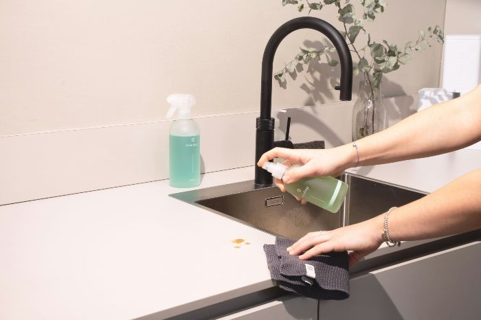 Vegan Cleaning Products And The Hidden Shifts They Trigger Indoors 4 Hand using a plant based cleaning spray on a kitchen counter in a London home