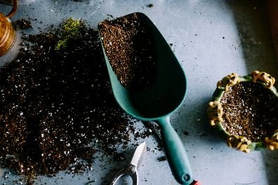 A close-up image of gardening essentials, including a soil-filled scoop and pruning shears, resting on a table scattered with soil, symbolizing the hands-on expertise and readiness of Samyx's gardening services.